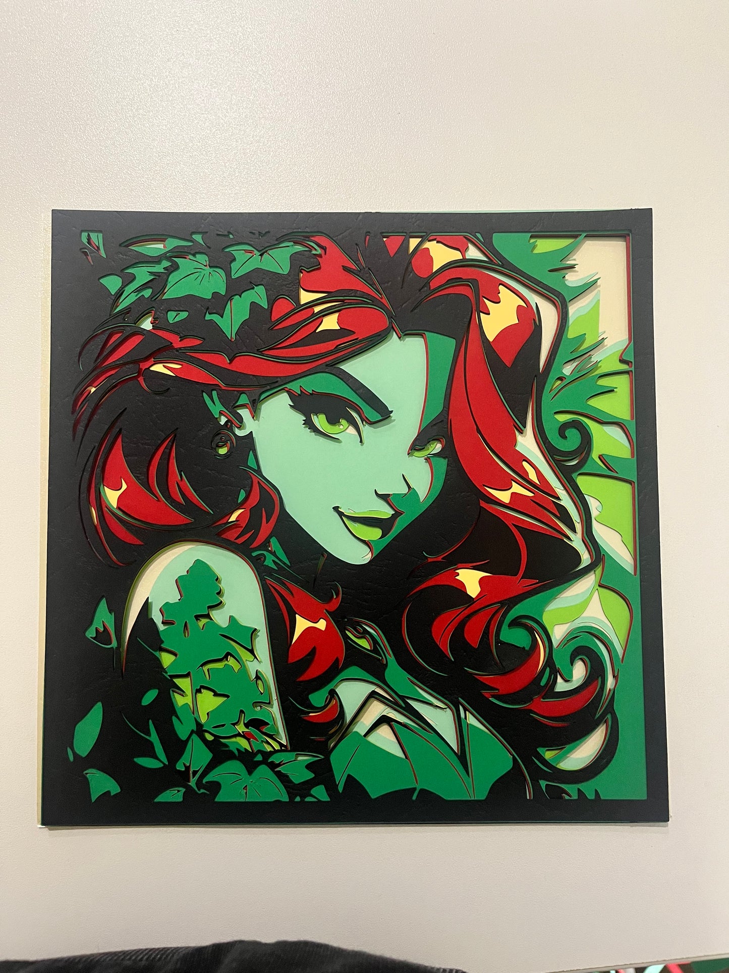 Višeslojna papercut zidna dekoracija Poison Ivy iz DC Comics-a – zelena koža, crvena kosa, bršljanovo lišće, crni okvir, frontalni prikaz na zidu