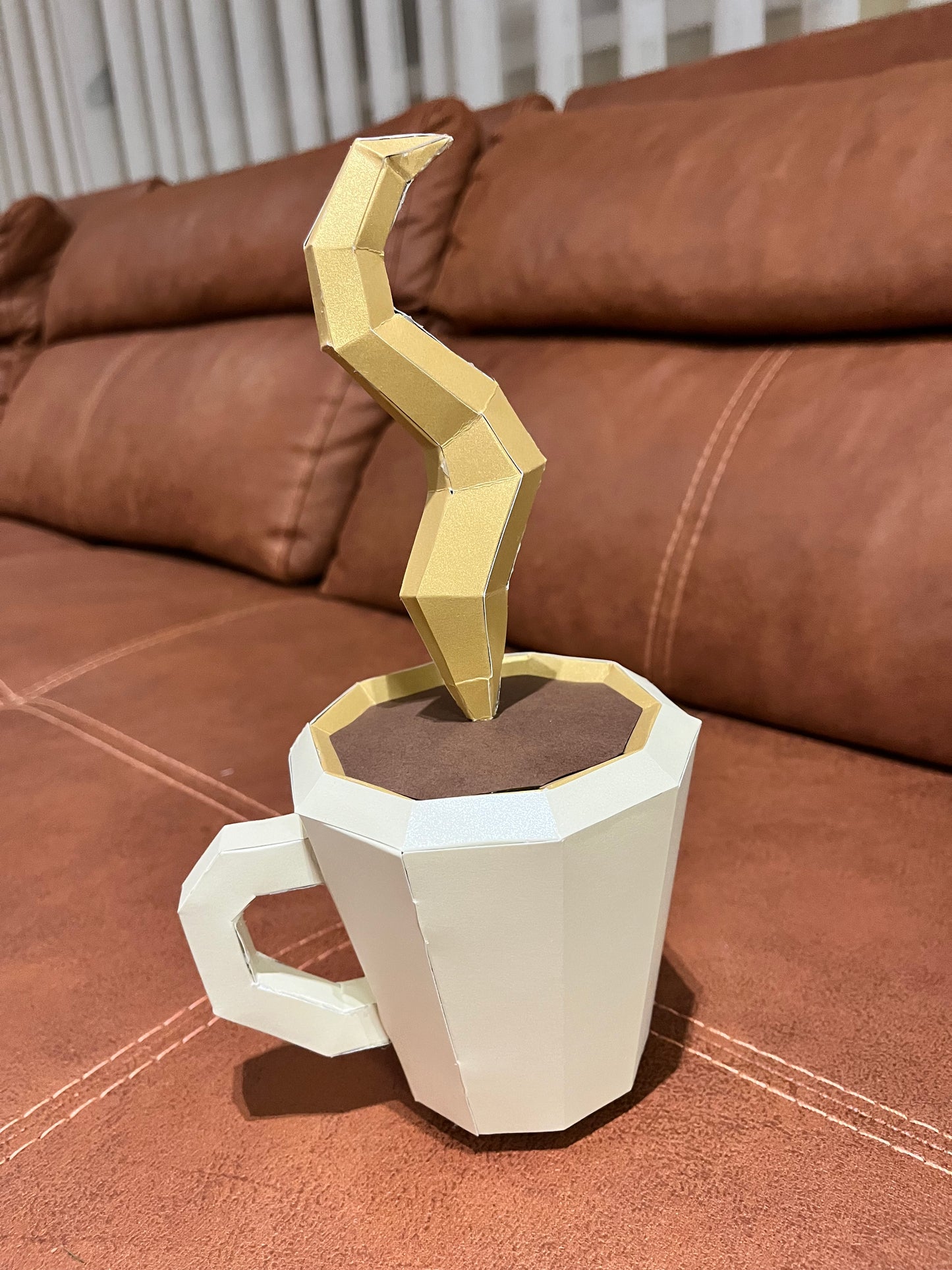 Bočni ugao low poly 3D skulpture šolje kafe – detalj geometrijske zlatne pare i braon površine kafe, papercraft izrada