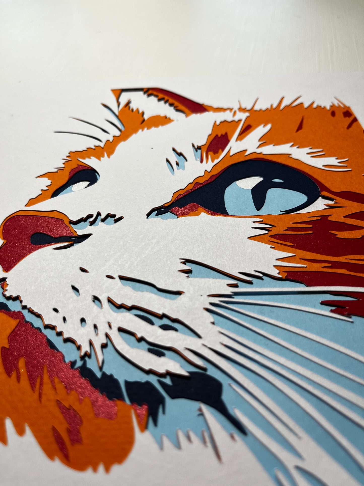 Detalj ručno rađene 3D papercut dekoracije riđe mačke – slojevi kartona sa plavim očima