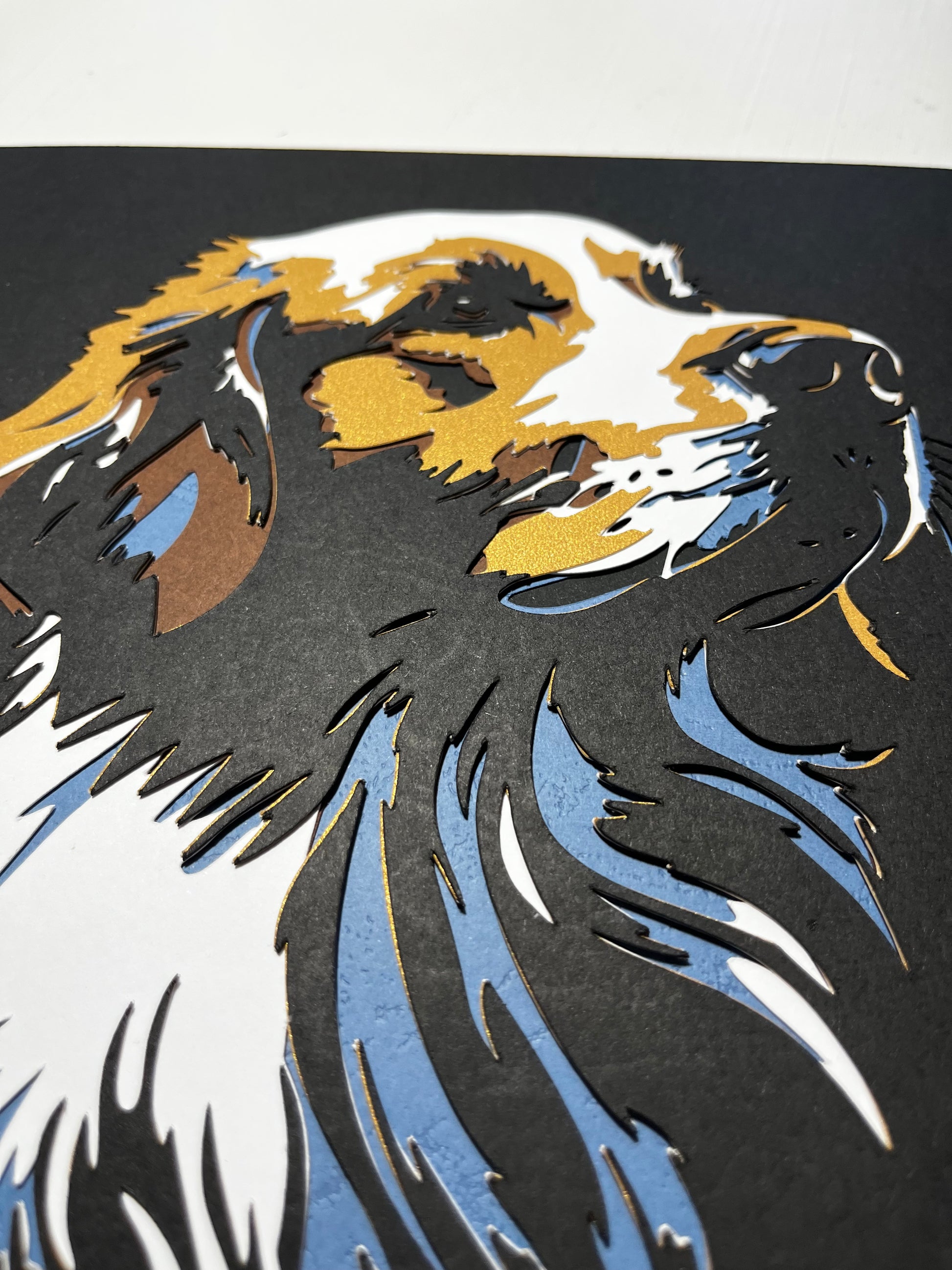 Detalj ručno rađene 3D papercut dekoracije psa – zlatni i plavi slojevi kartona na crnoj pozadini