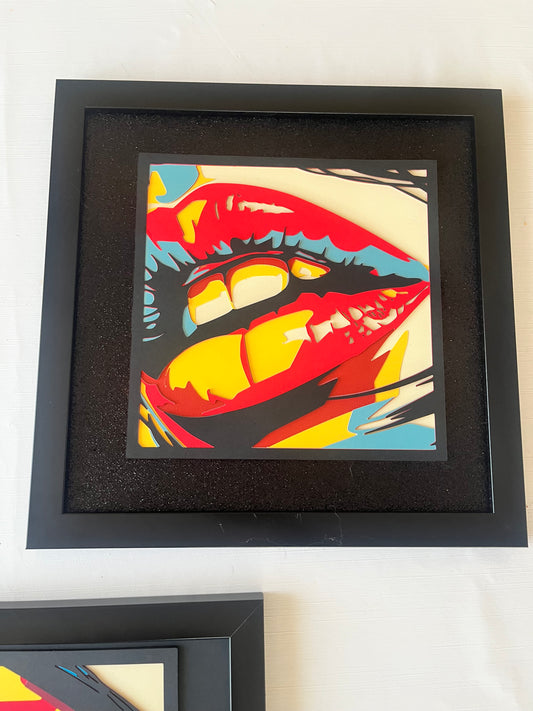 Uokvirena pop art slika usana u crnom okviru sa crvenim, žutim i plavim detaljima