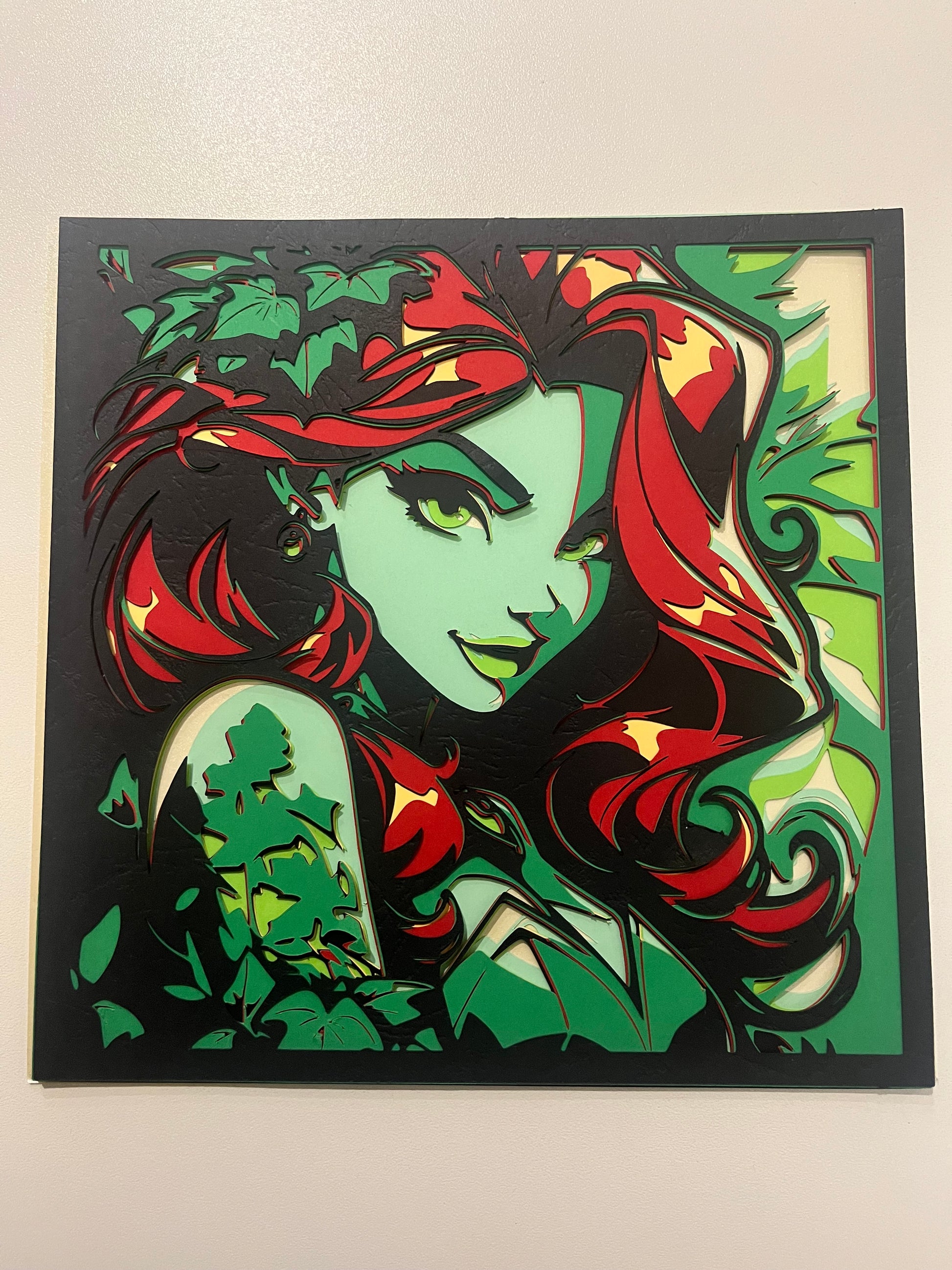 Krupniji prikaz višeslojne papercut dekoracije Poison Ivy – detalj precizno izrezanih slojeva zelenog lišća i crvene kose u crnom okviru