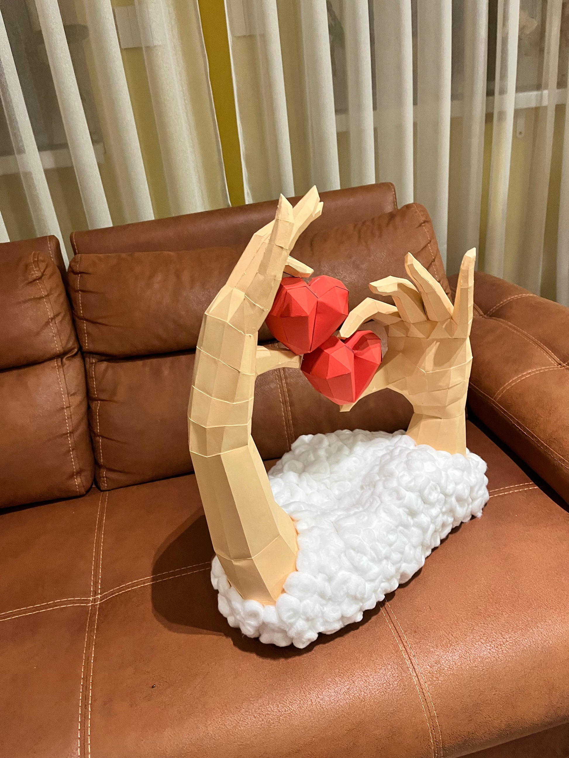 Low poly 3D skulptura ruku sa srcima na braon kožnoj sofi, bočni ugao, prikaz dimenzija i bele osnove od vate