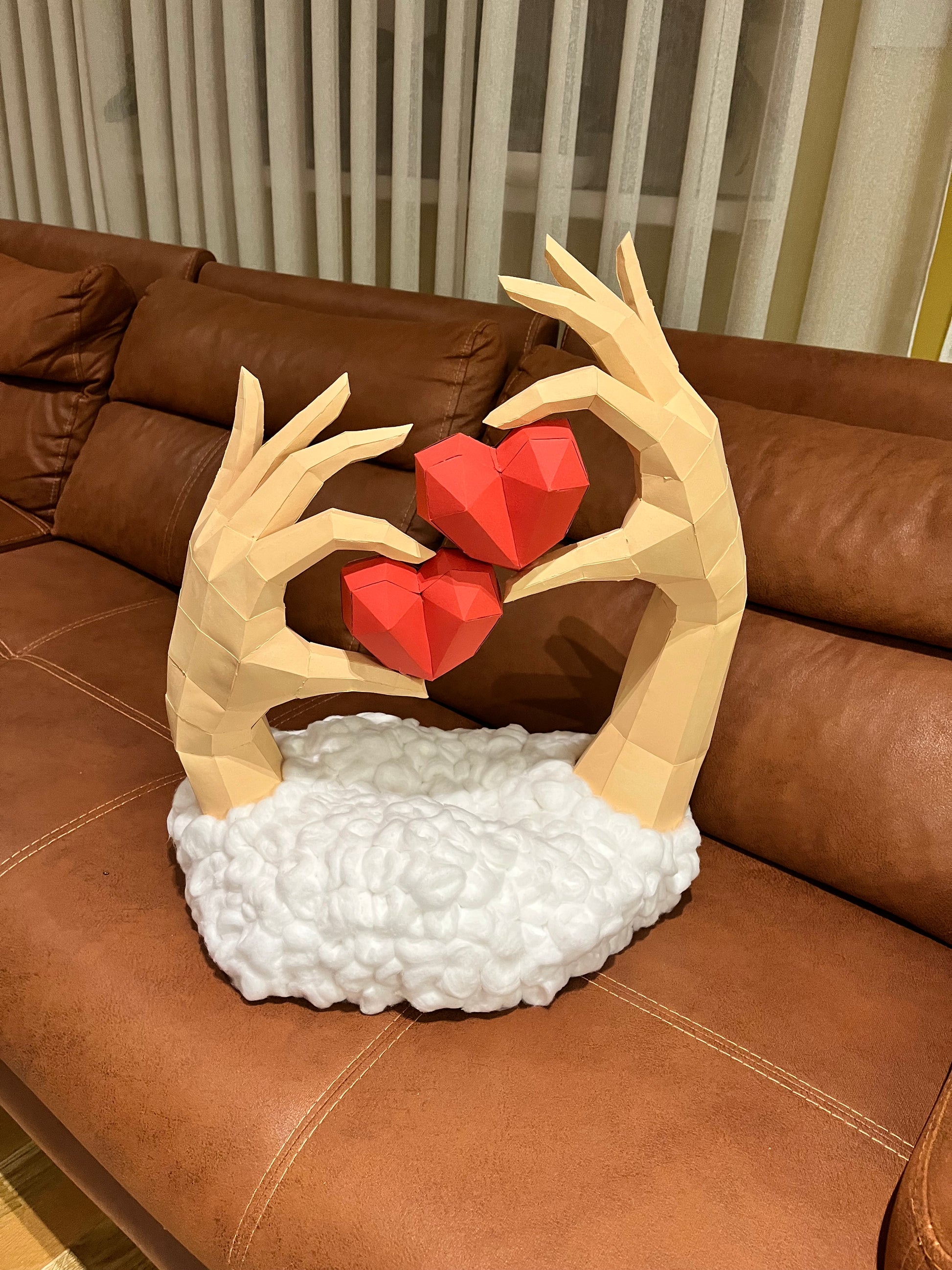 Low poly 3D skulptura ruku sa srcima, perspektivni ugao na kožnoj sofi – prikaz dubine i trodimenzionalnosti