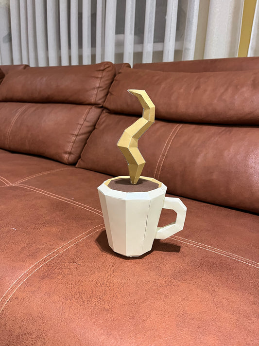 Low poly 3D papercraft skulptura bele šolje kafe sa zlatnom geometrijskom parom, lifestyle prikaz na braon kožnoj sofi