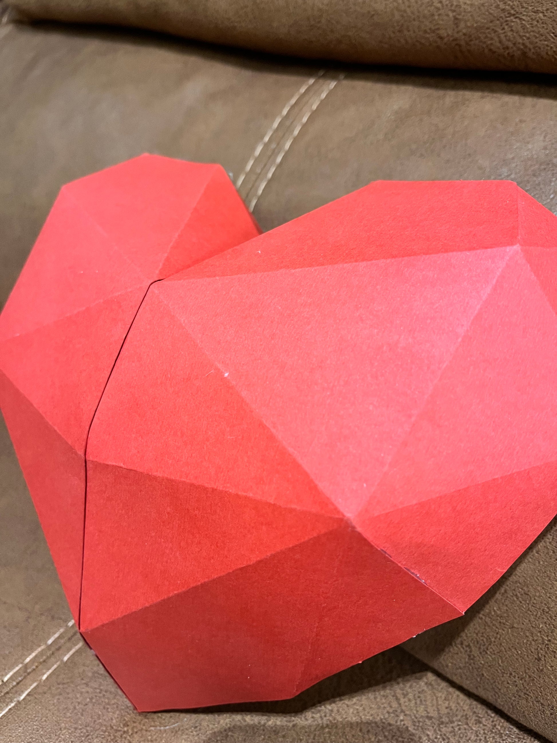 Bočni ugao low poly 3D papercraft skulpture srca na kožnoj sofi – prikaz dubine i geometrijskih slojeva papira