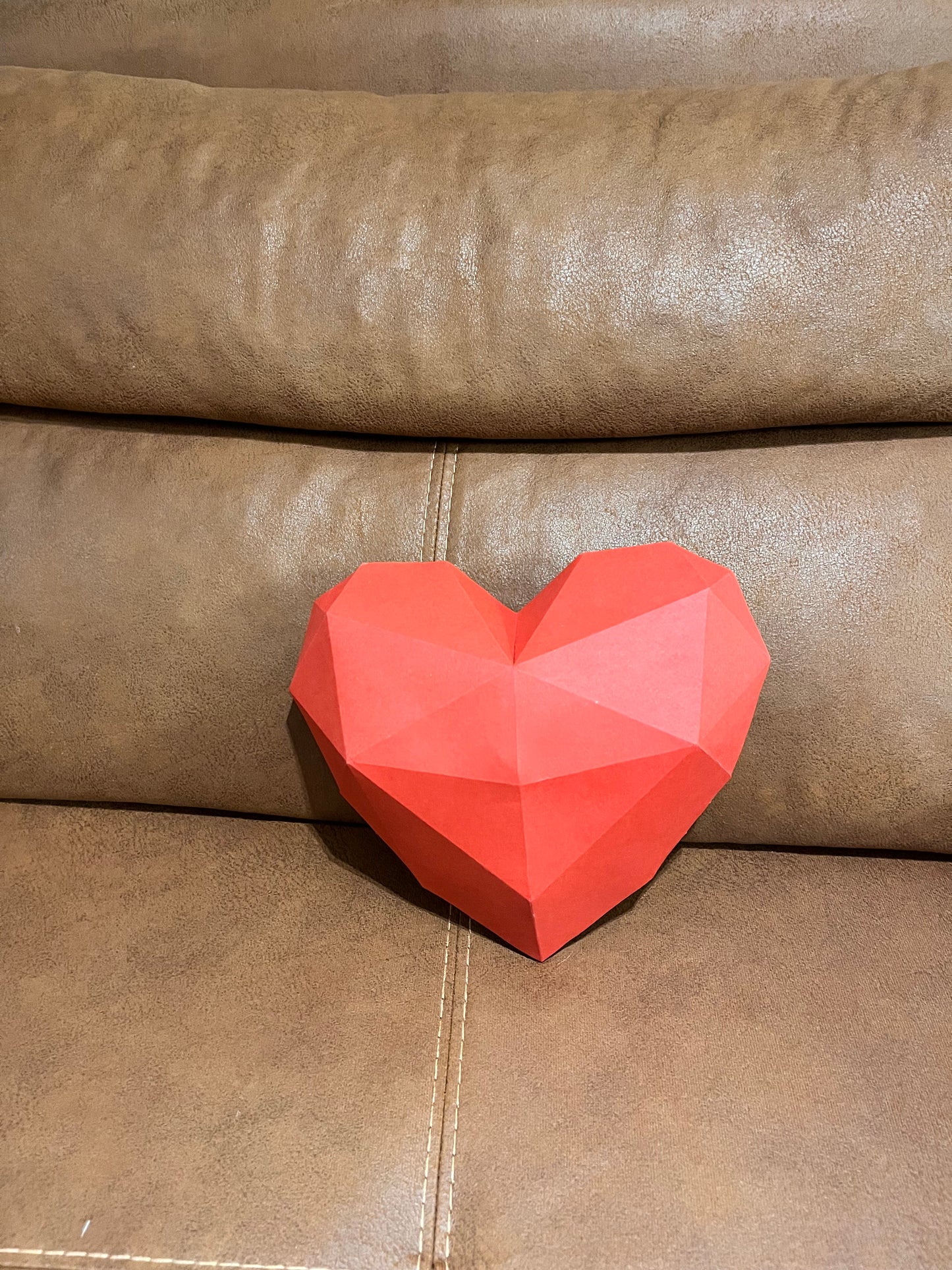 Low poly 3D papercraft skulptura crveno-roze srca na braon kožnoj sofi, frontalni prikaz, romantični poklon