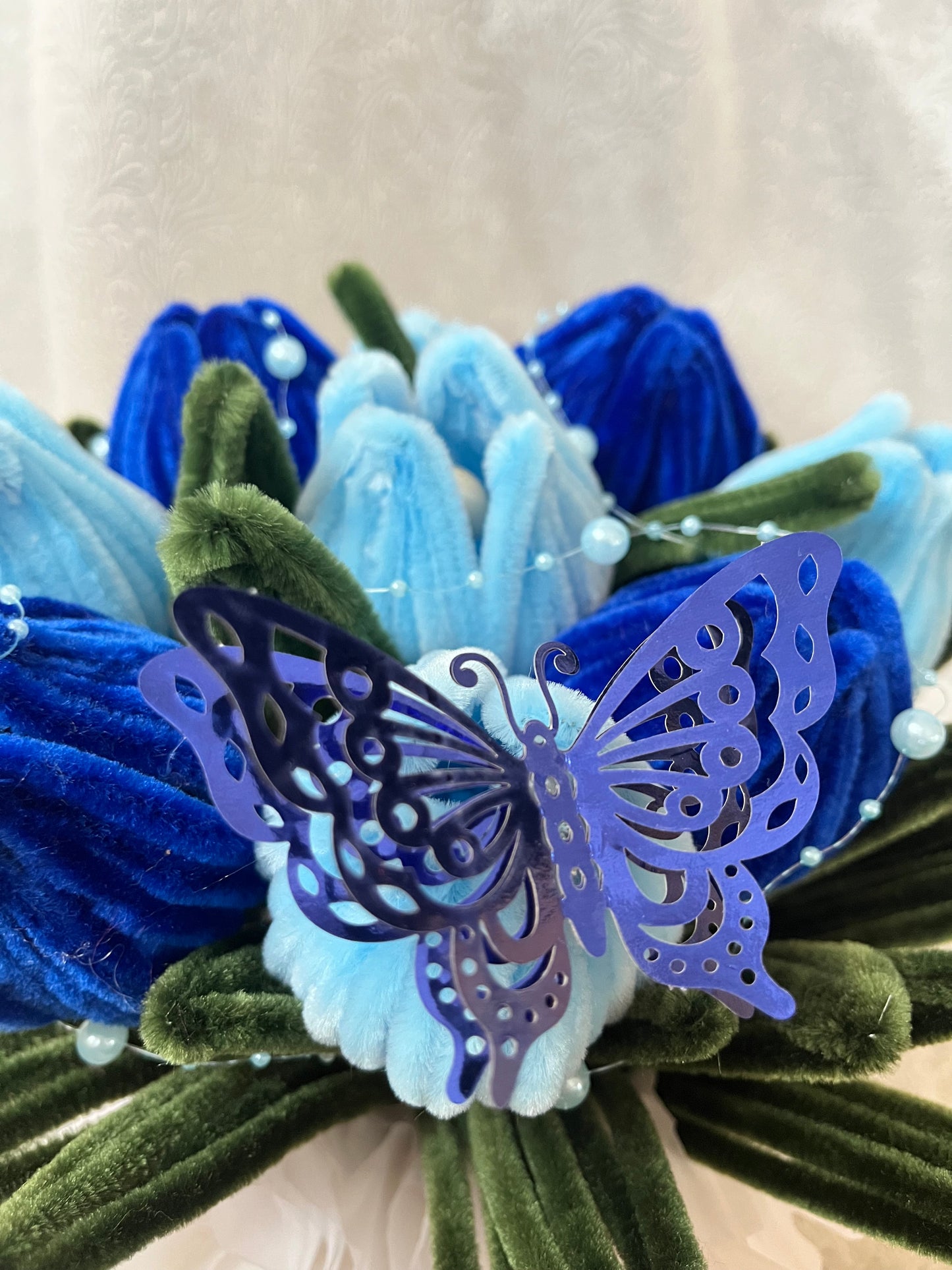 Detalj plišanih plavih lala sa dekorativnim ljubičastim leptirom i perlicama