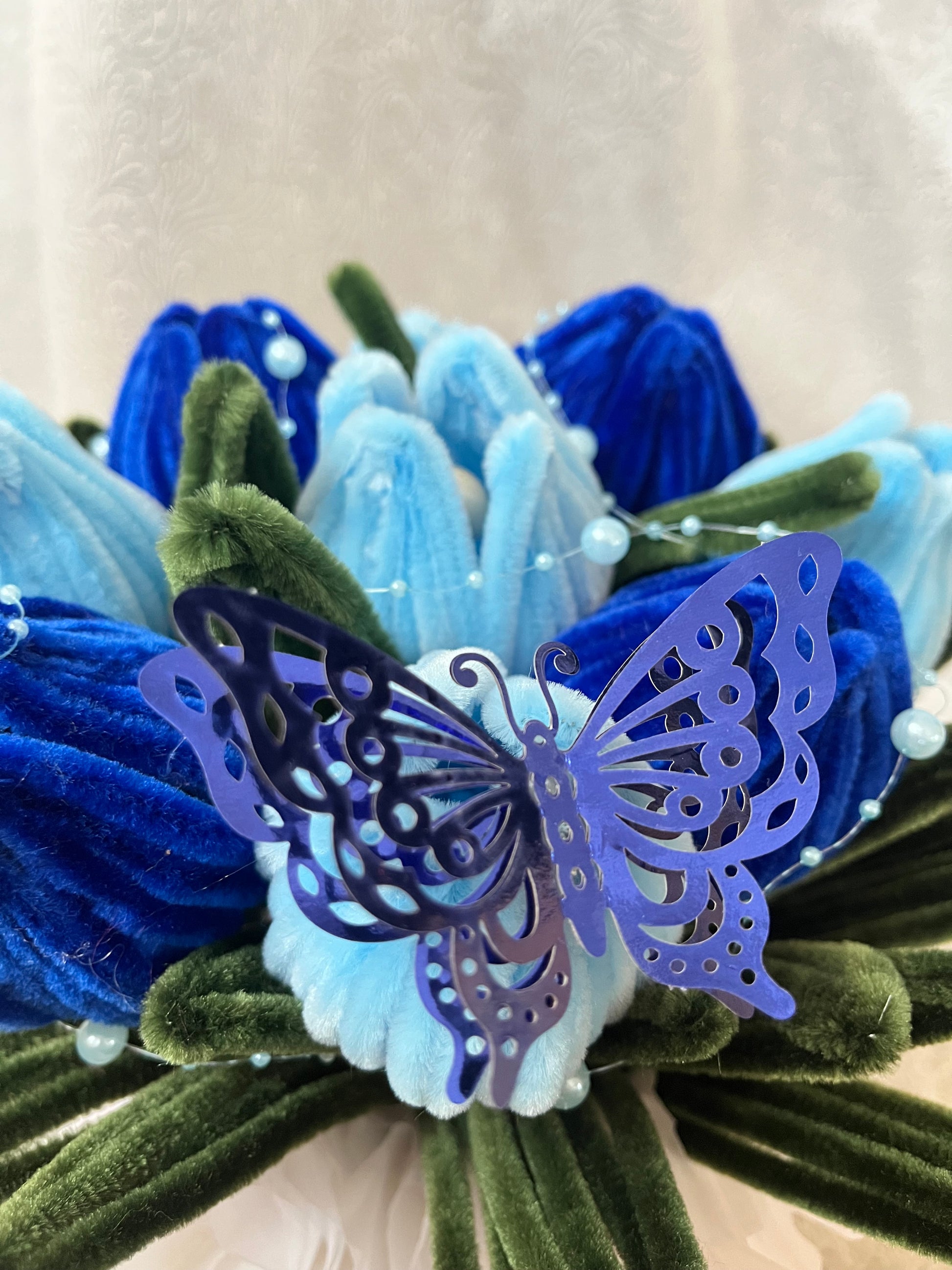 Detalj plišanih plavih lala sa dekorativnim ljubičastim leptirom i perlicama
