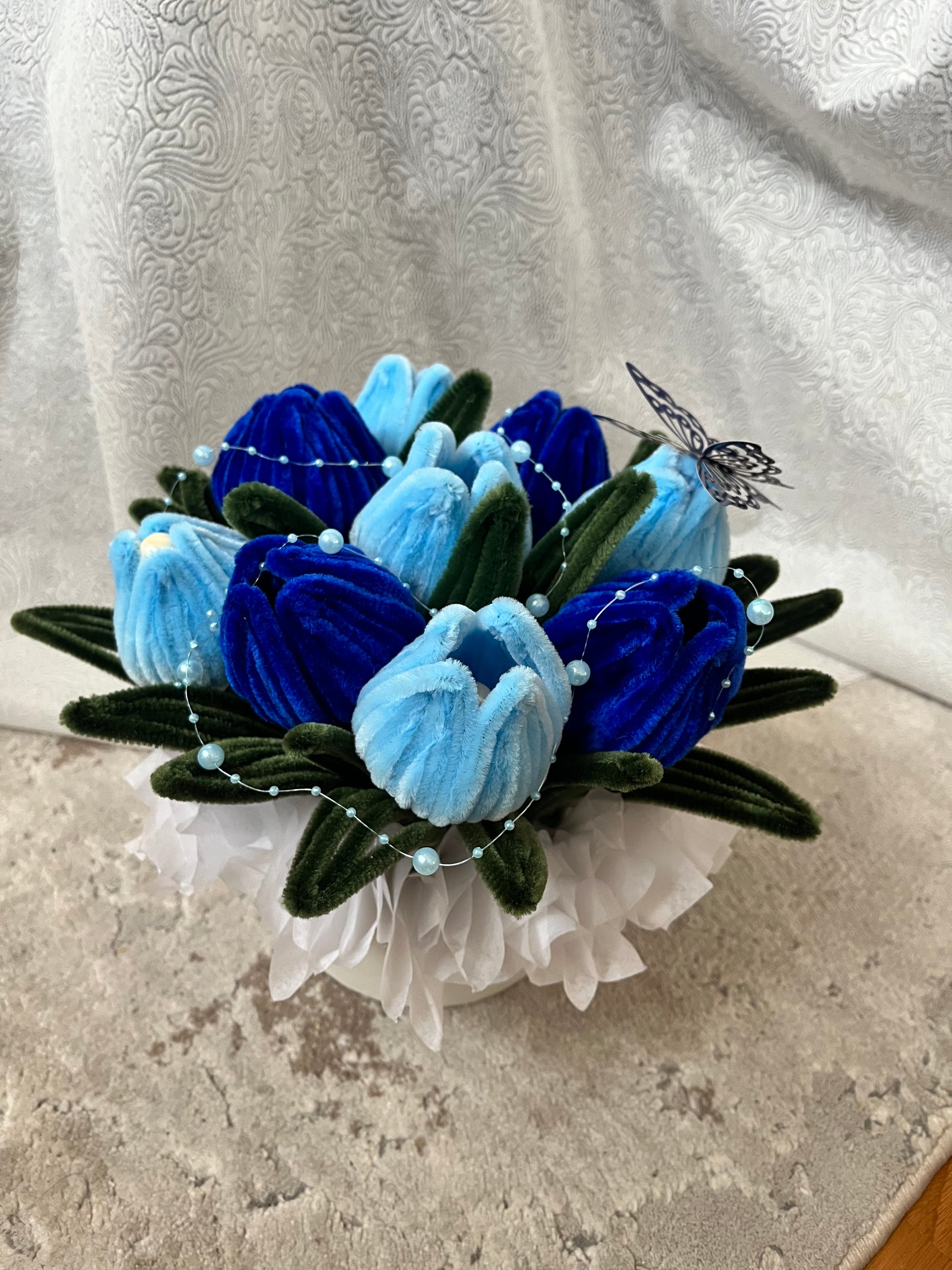 Detalj plišanog buketa lala odozgo, plave i svetloplave lale sa dekorativnim leptirom