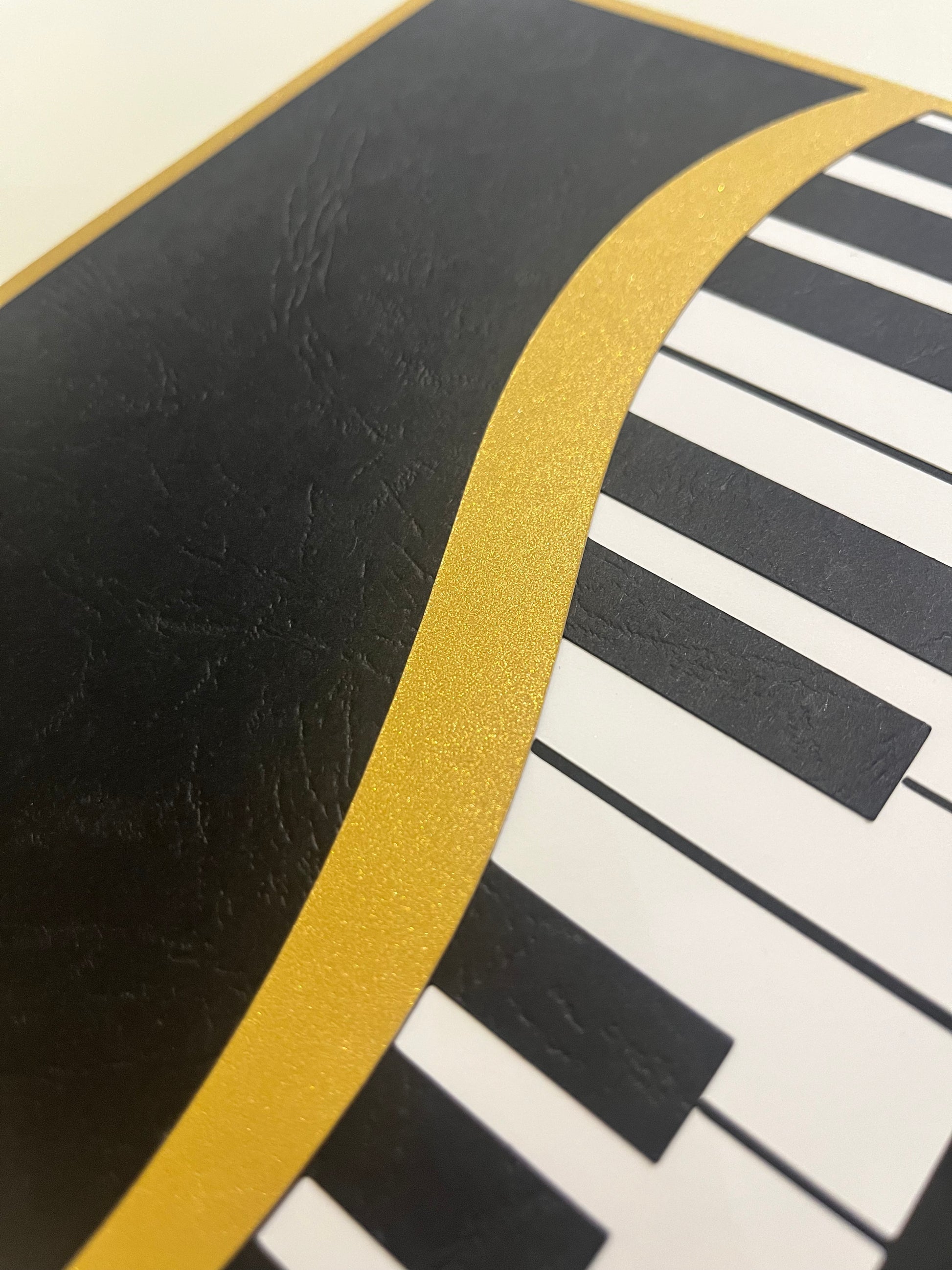 Krupni plan zlatne metalik linije i precizno izrezanih klavirskih dirki na 3D shadow box okviru