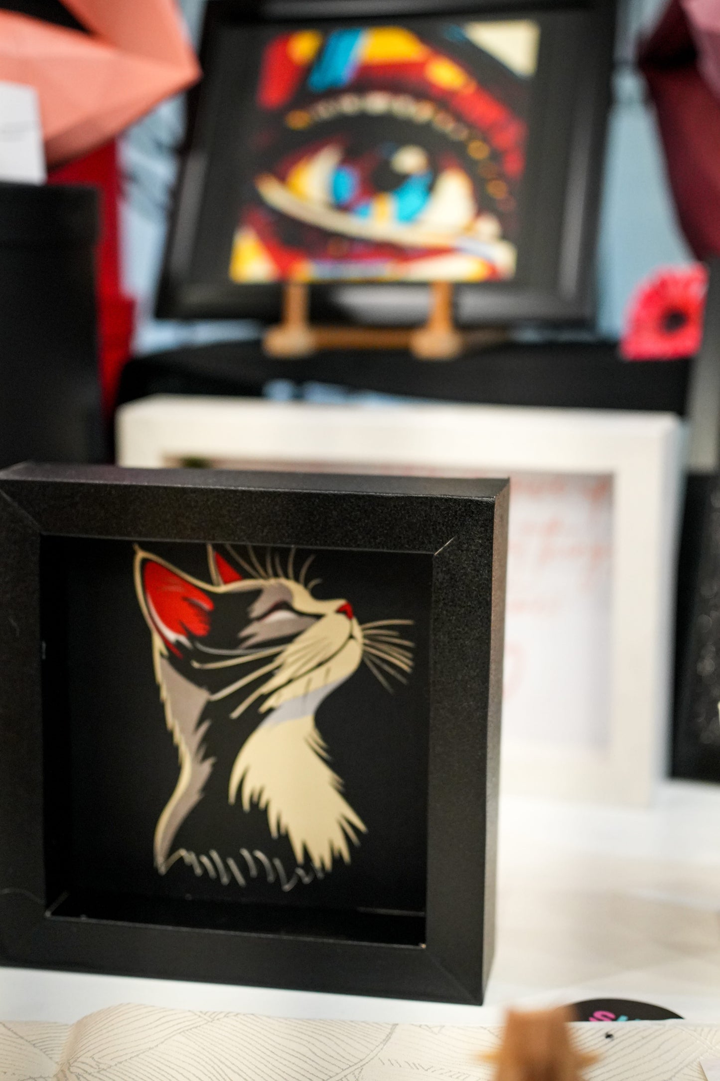 3D shadow box sa višeslojnim papercut portretom mačke u crnom okviru, lifestyle prikaz sa više umetničkih dela u pozadini